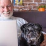 older man with old pug and laptop computer