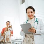 female veterinarian holds a tablet with her male client and dog patient in the background