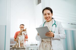 female veterinarian holds a tablet with her male client and dog patient in the background